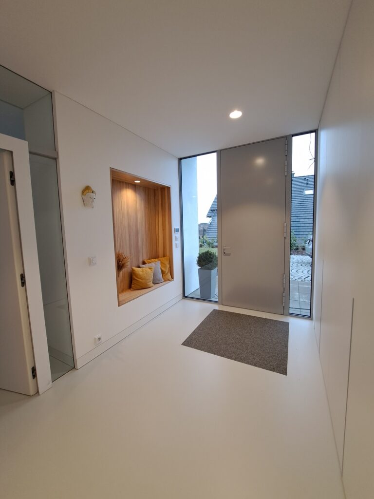 Elegantní vestavěná skříň se sezením v rodinném domě. Sestava je z bílého matného lamina v kombinaci s dřevodekorem. Všechna dvířka jsou otevírací do boku pomocí bezúchytkového systému TIP ON.