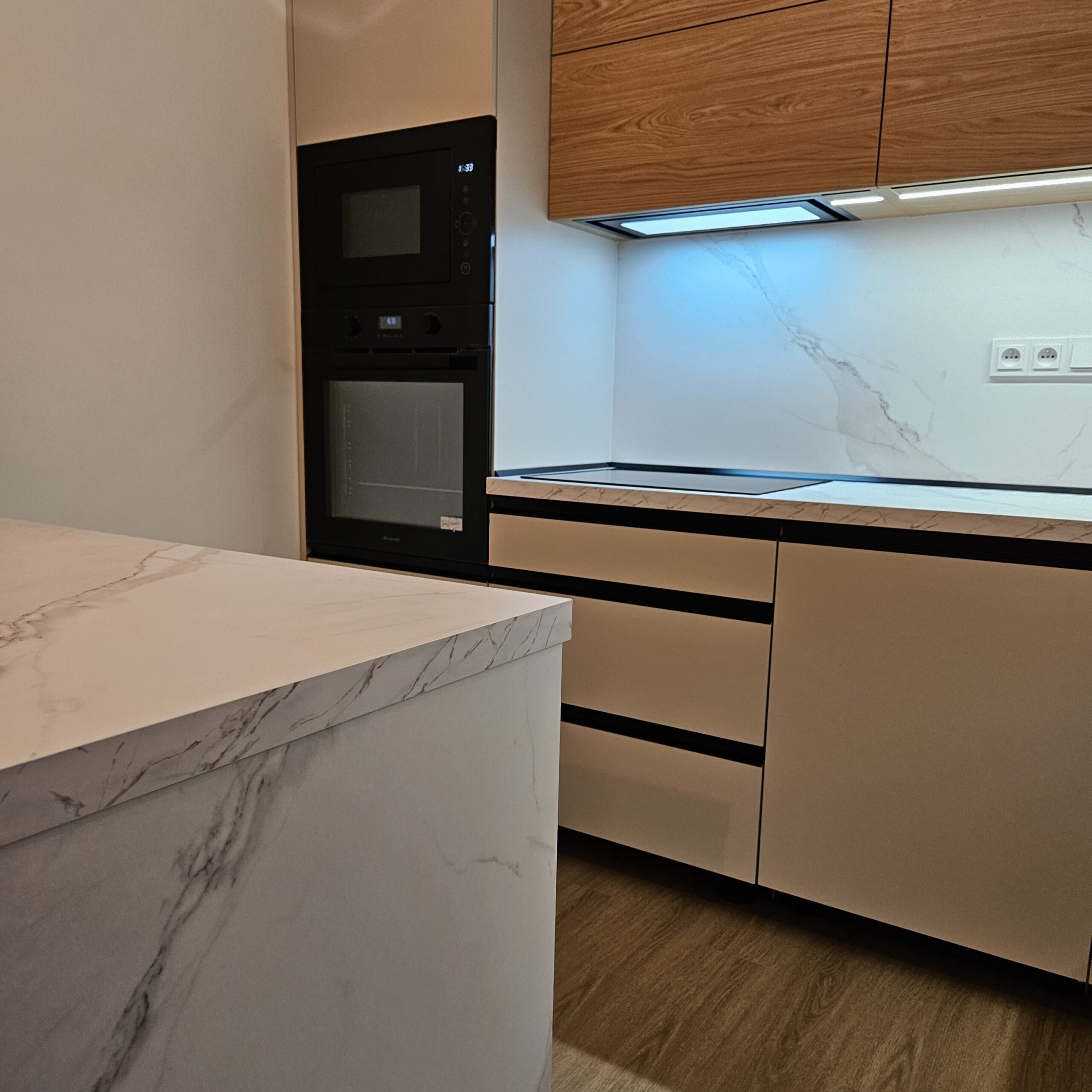 Tato kuchyň na míru propojuje jemný, klidný tón kašmírové šedé s přírodní kresbou dřevodekoru, díky čemuž vzniká prostor, který působí elegantně, útulně a nadčasově. Turnov, Rychnov, Jablonec nad Nisou, Liberec, Kokonín.