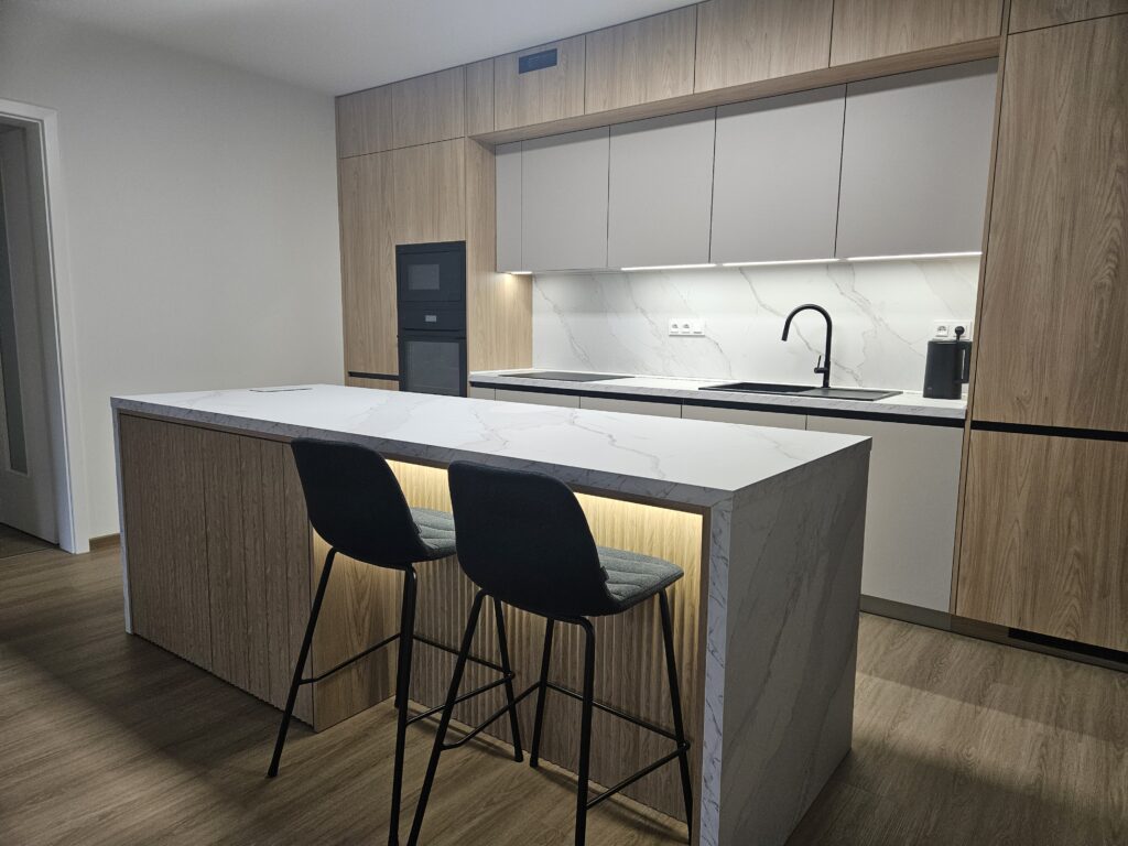 Moderní kuchyň pro mladou rodinu v Jablonci nad Nisou - Kokonín Zvolená kombinace materiálů a barev vytváří klidný a elegantní celek, zatím co precizní zpracování, kvalitní kování a praktické zafrézované úchytky podtrhují nadčasový charakter této realizace. Součástí realizace byl také pracovní kout ve stejném materiálovém provedení.